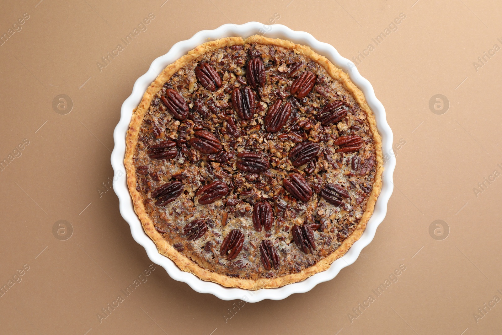 Photo of Delicious pecan pie in baking dish on light brown background, top view