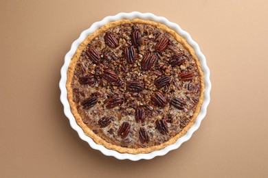 Delicious pecan pie in baking dish on light brown background, top view