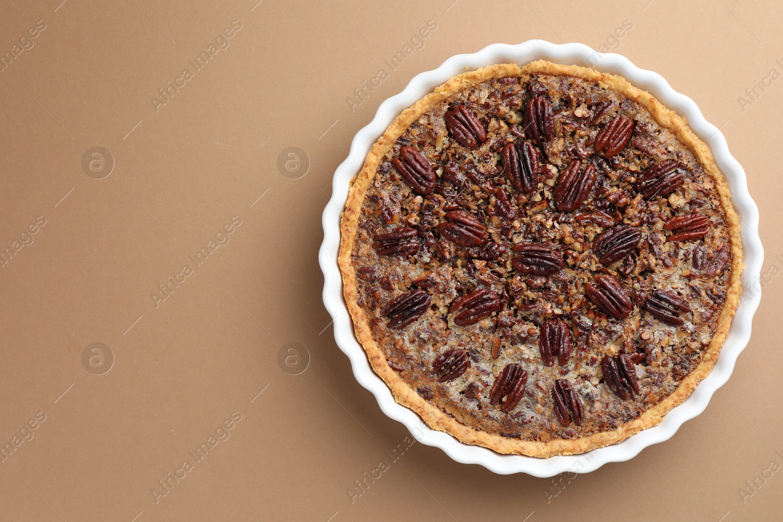 Photo of Delicious pecan pie in baking dish on light brown background, top view. Space for text