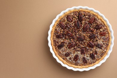 Delicious pecan pie in baking dish on light brown background, top view. Space for text