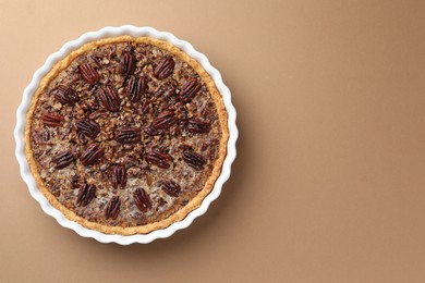 Photo of Delicious pecan pie in baking dish on light brown background, top view. Space for text