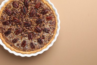 Photo of Delicious pecan pie in baking dish on light brown background, top view. Space for text