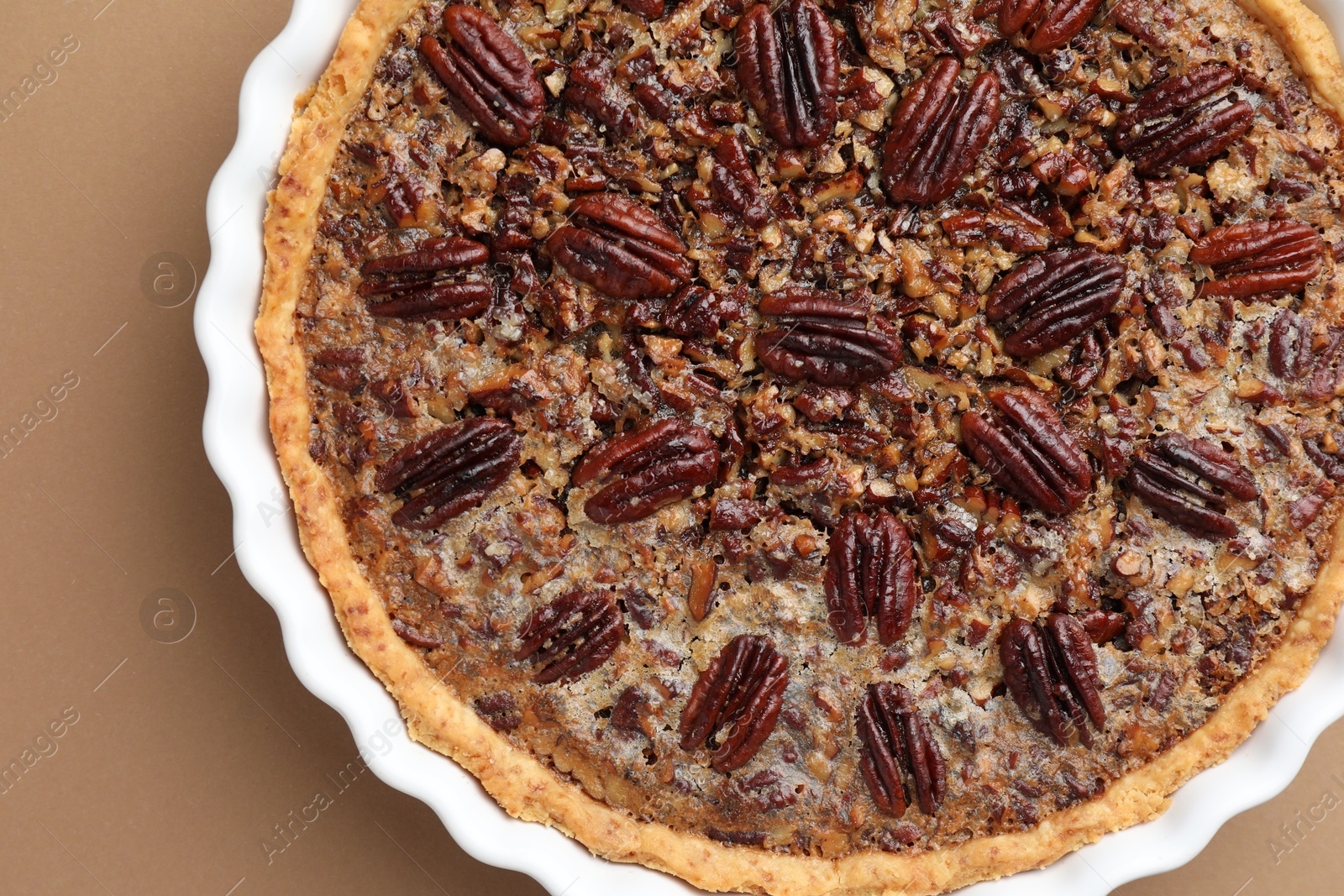 Photo of Delicious pecan pie in baking dish on light brown background, top view