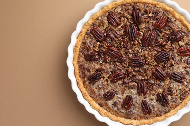 Delicious pecan pie in baking dish on light brown background, top view. Space for text