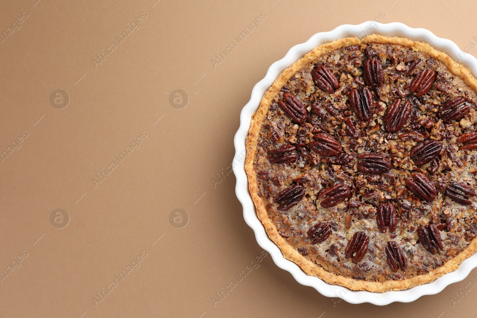 Photo of Delicious pecan pie in baking dish on light brown background, top view. Space for text