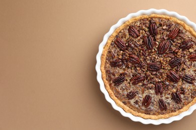 Delicious pecan pie in baking dish on light brown background, top view. Space for text