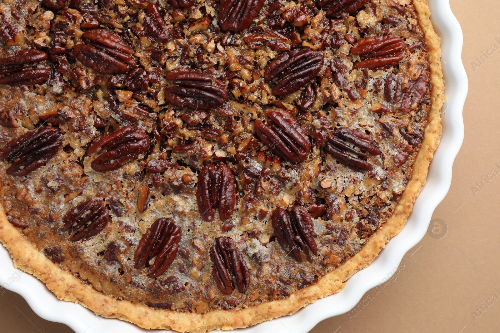 Photo of Delicious pecan pie in baking dish on light brown background, top view