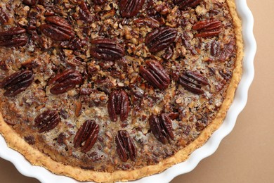 Delicious pecan pie in baking dish on light brown background, top view