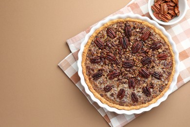 Delicious pecan pie in baking dish and fresh nuts on light brown background, flat lay. Space for text