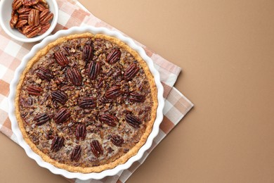 Delicious pecan pie in baking dish and fresh nuts on light brown background, flat lay. Space for text