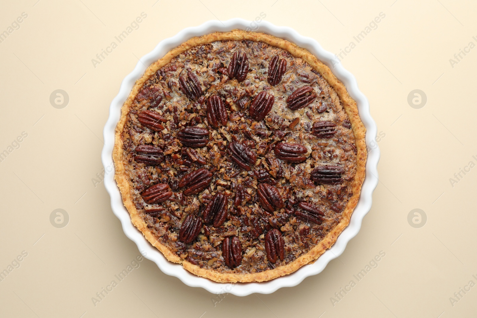 Photo of Delicious pecan pie in baking dish on beige background, top view