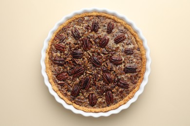 Delicious pecan pie in baking dish on beige background, top view