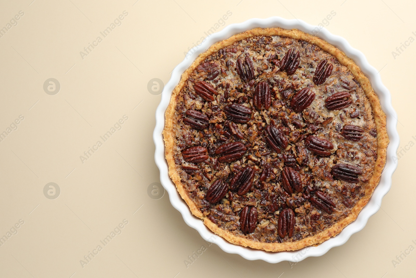 Photo of Delicious pecan pie in baking dish on beige background, top view. Space for text