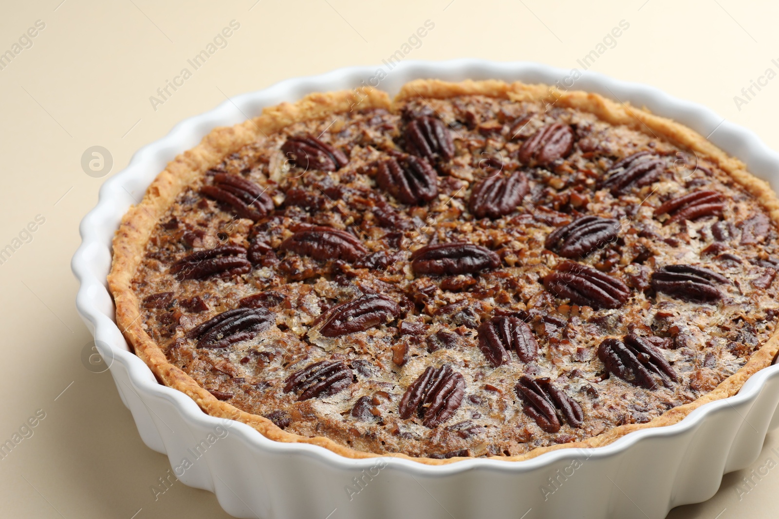 Photo of Delicious pecan pie in baking dish on beige background, closeup