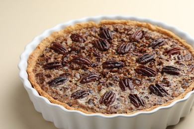 Photo of Delicious pecan pie in baking dish on beige background, closeup