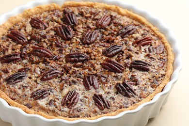 Delicious pecan pie in baking dish on beige background, closeup