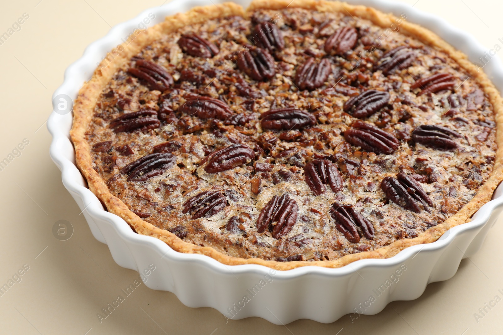 Photo of Delicious pecan pie in baking dish on beige background, closeup