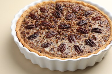 Photo of Delicious pecan pie in baking dish on beige background, closeup