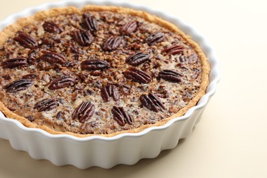 Delicious pecan pie in baking dish on beige background, closeup