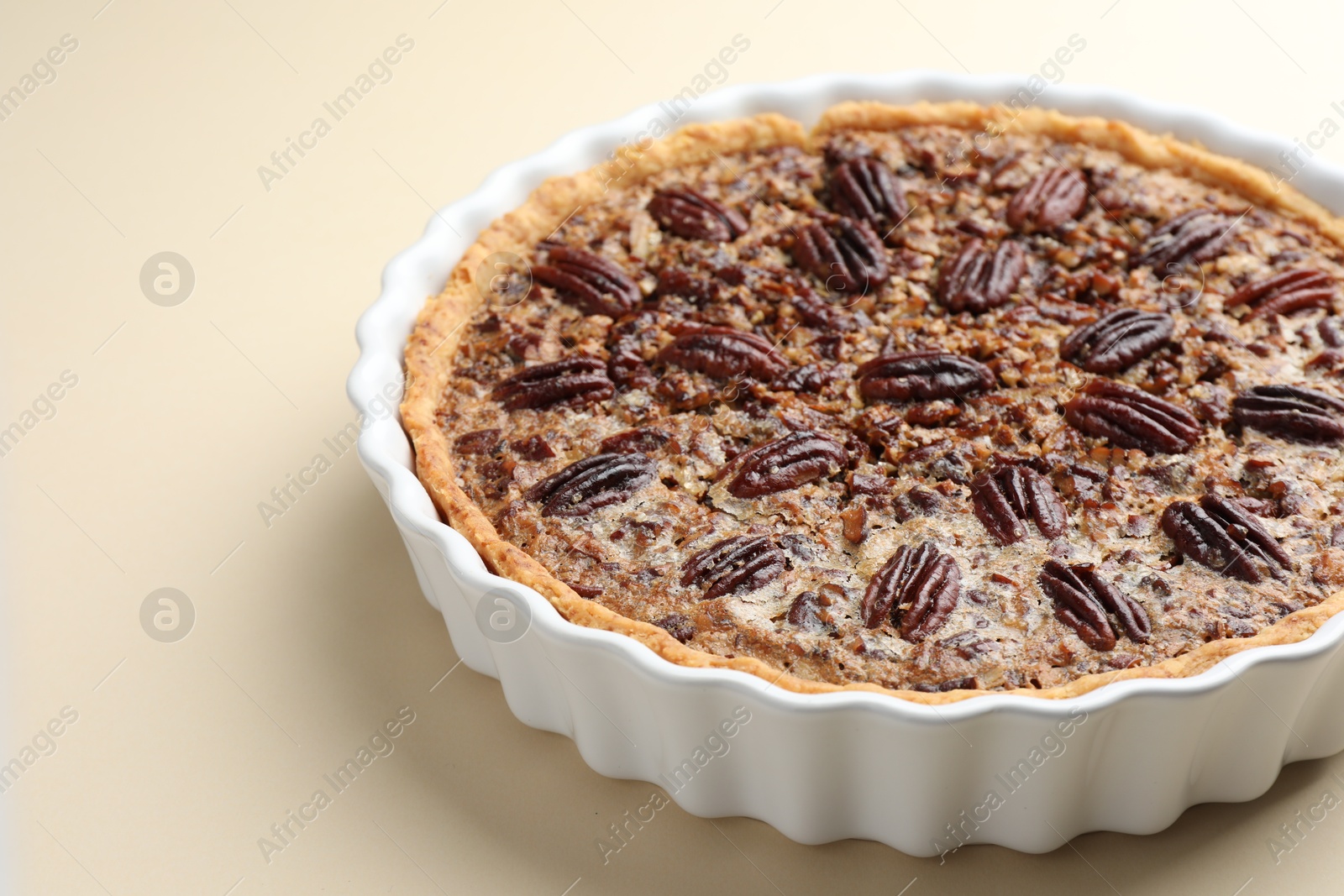 Photo of Delicious pecan pie in baking dish on beige background, closeup