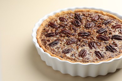 Photo of Delicious pecan pie in baking dish on beige background, closeup