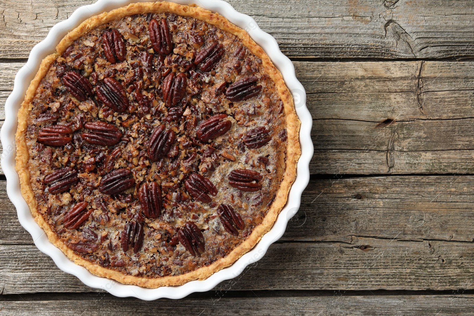 Photo of Delicious pecan pie in baking dish on wooden table, top view. Space for text