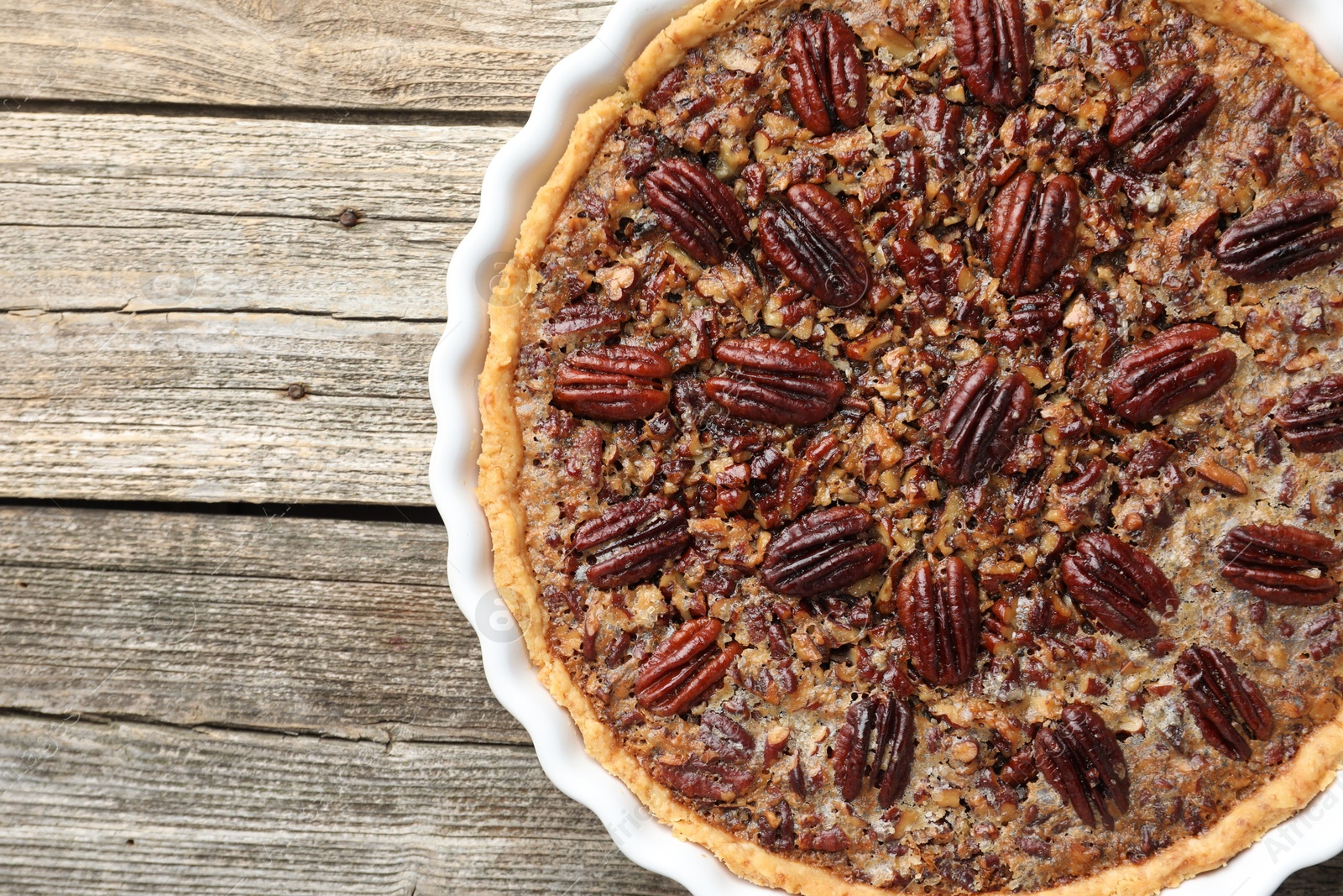 Photo of Delicious pecan pie in baking dish on wooden table, top view