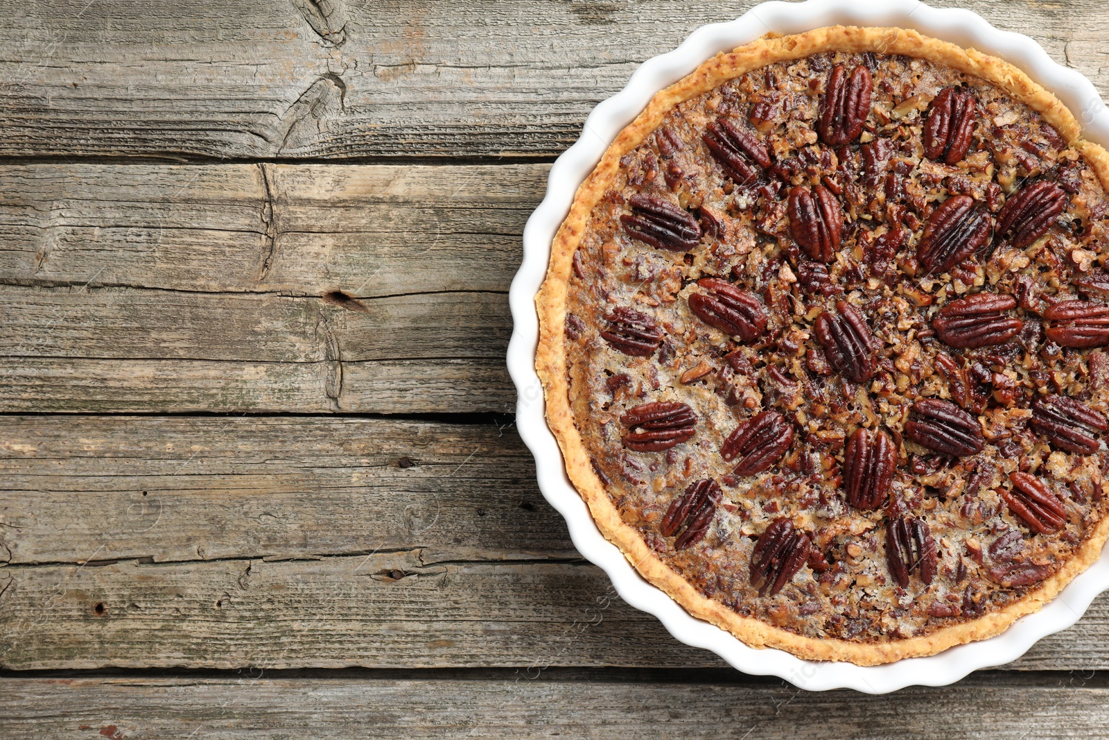 Photo of Delicious pecan pie in baking dish on wooden table, top view. Space for text