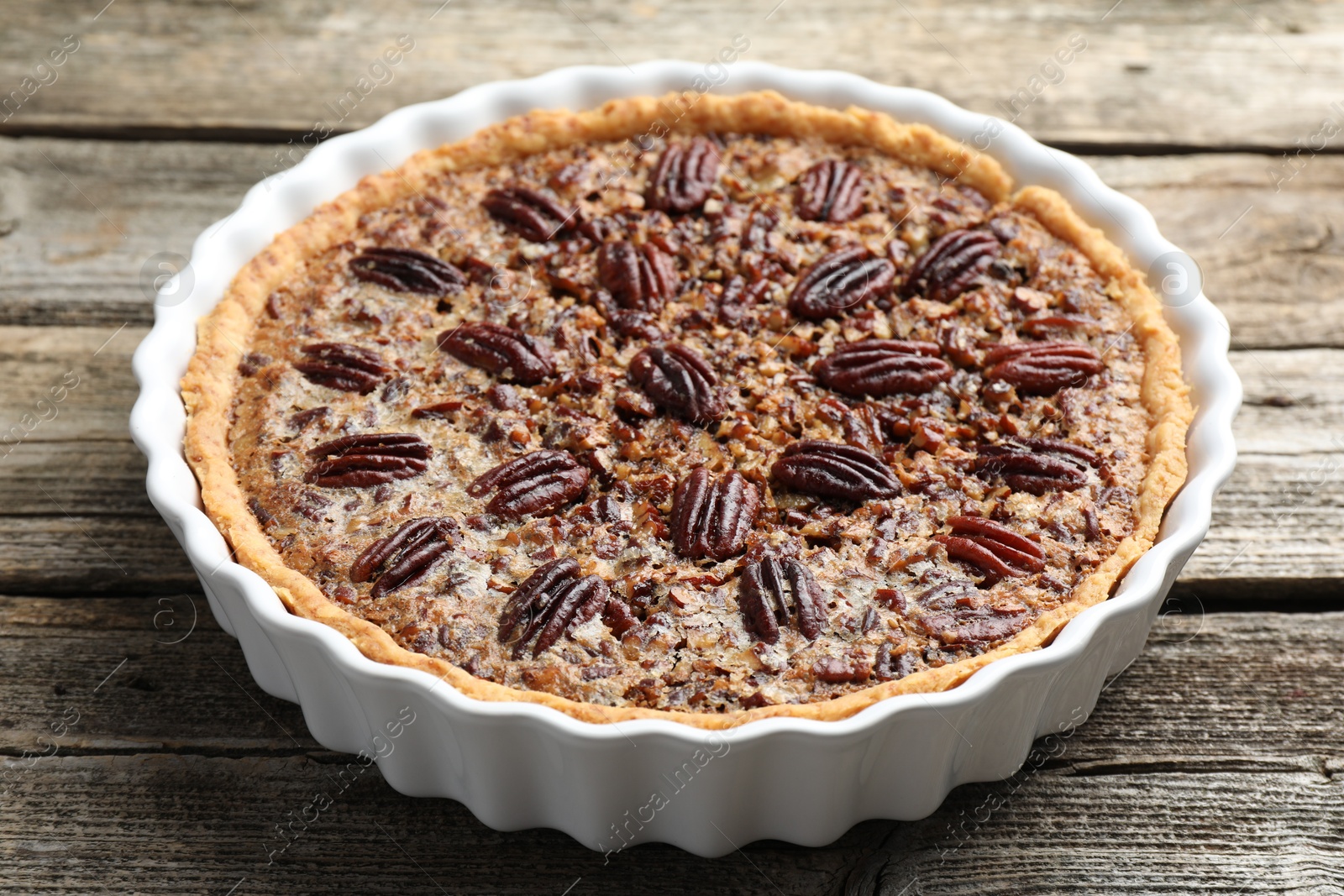 Photo of Delicious pecan pie in baking dish on wooden table, closeup