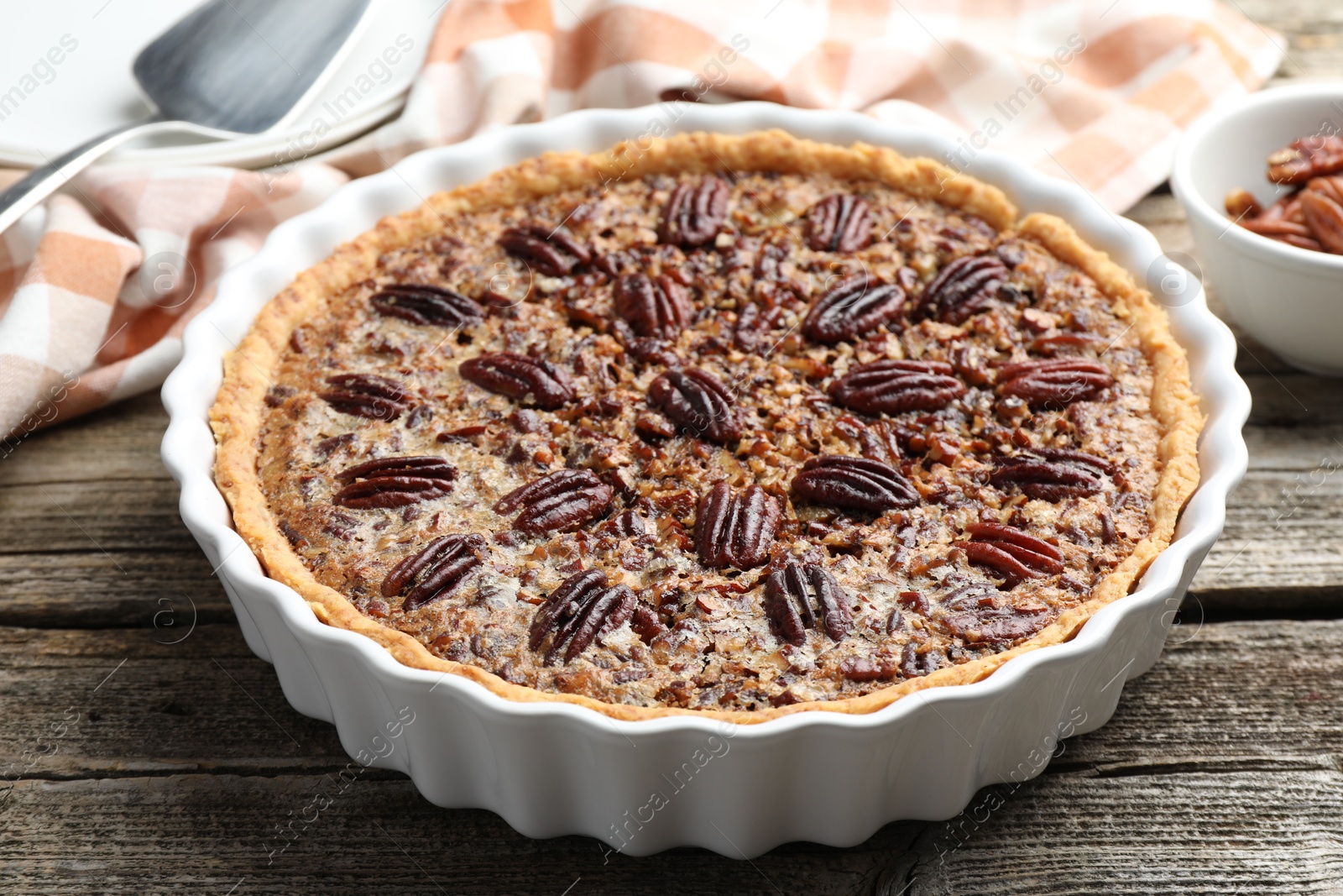 Photo of Delicious pecan pie in baking dish on wooden table, closeup