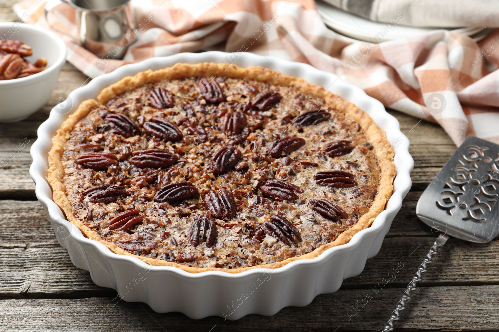 Photo of Delicious pecan pie in baking dish and cake server on wooden table, closeup