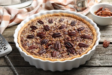 Photo of Delicious pecan pie in baking dish and cake server on wooden table, closeup