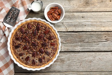 Delicious pecan pie in baking dish, fresh nuts, milk and cake server on wooden table, flat lay. Space for text