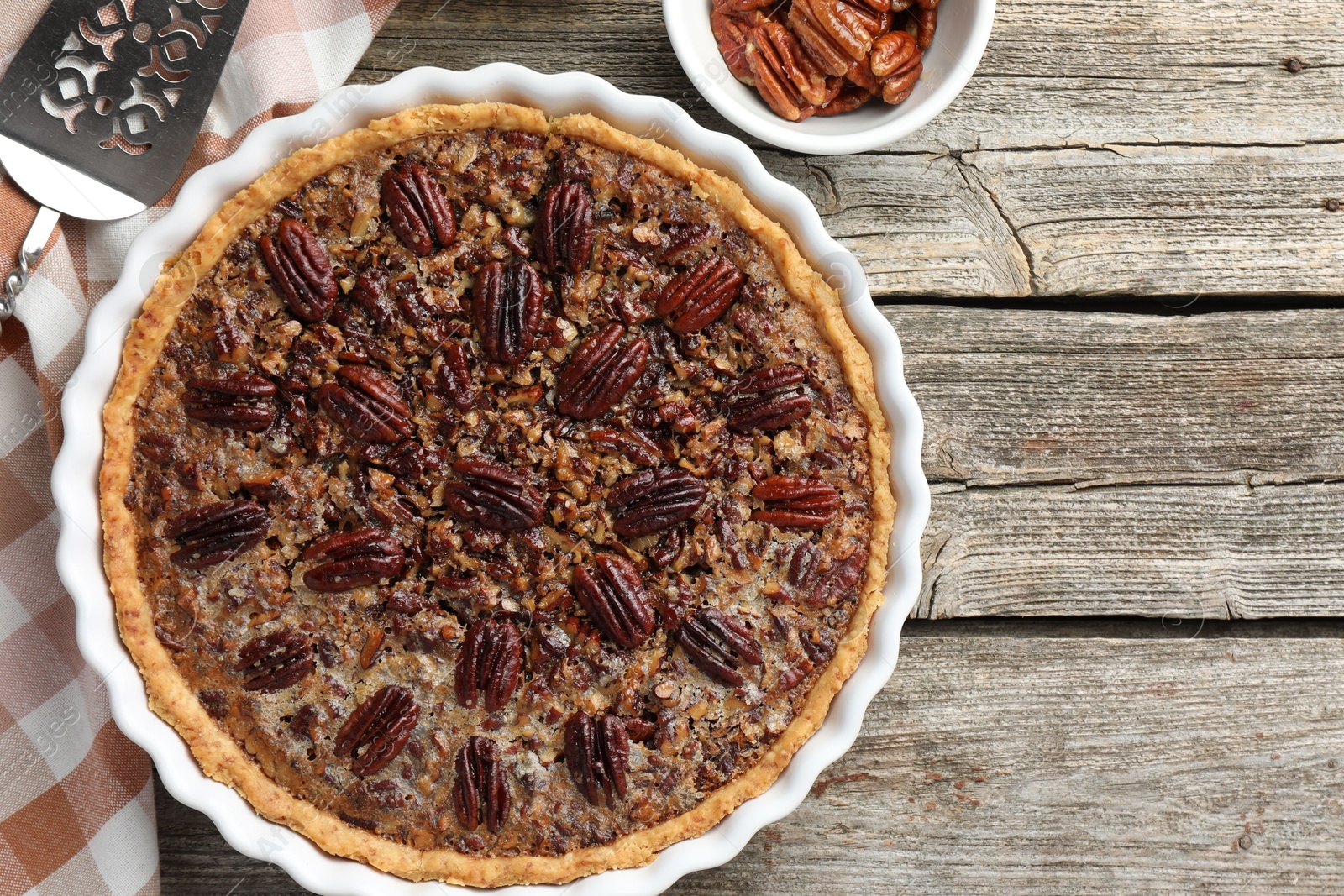 Photo of Delicious pecan pie in baking dish, fresh nuts and cake server on wooden table, flat lay. Space for text