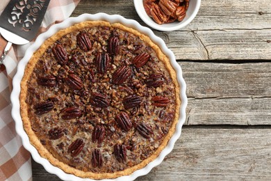 Photo of Delicious pecan pie in baking dish, fresh nuts and cake server on wooden table, flat lay. Space for text