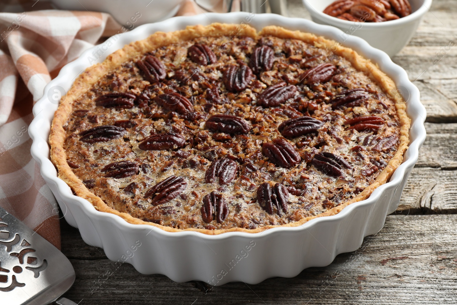 Photo of Delicious pecan pie in baking dish on wooden table, closeup