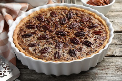 Photo of Delicious pecan pie in baking dish on wooden table, closeup