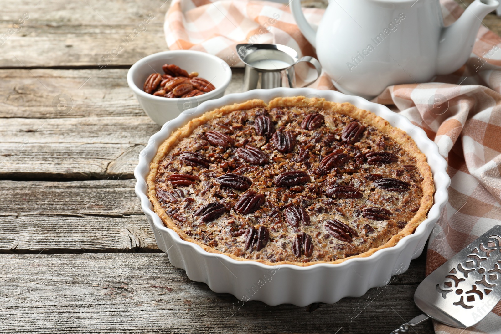 Photo of Delicious pecan pie in baking dish and cake server on wooden table, closeup