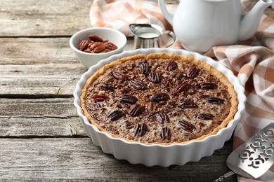 Delicious pecan pie in baking dish and cake server on wooden table, closeup