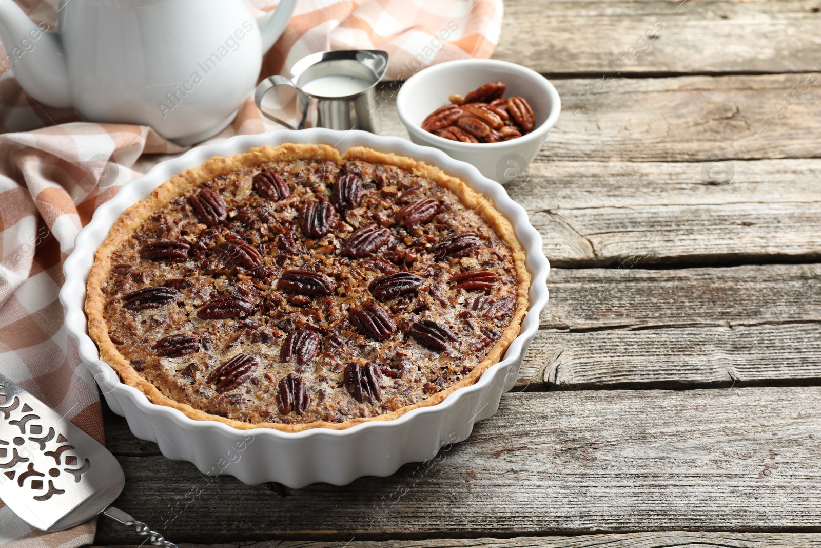 Photo of Delicious pecan pie in baking dish and cake server on wooden table, closeup. Space for text