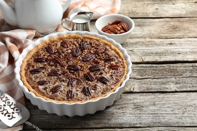 Delicious pecan pie in baking dish and cake server on wooden table, closeup. Space for text