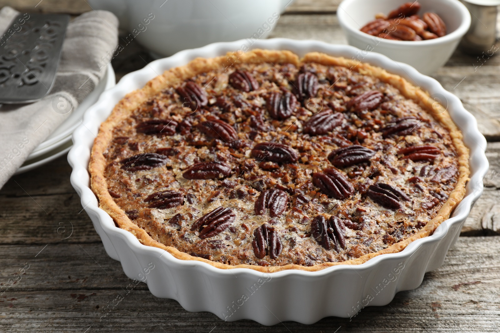 Photo of Delicious pecan pie in baking dish on wooden table, closeup