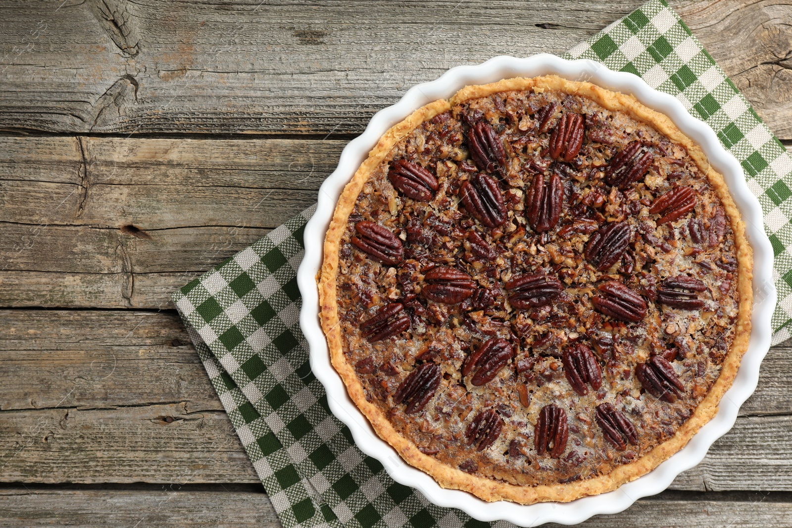 Photo of Delicious pecan pie in baking dish on wooden table, top view. Space for text