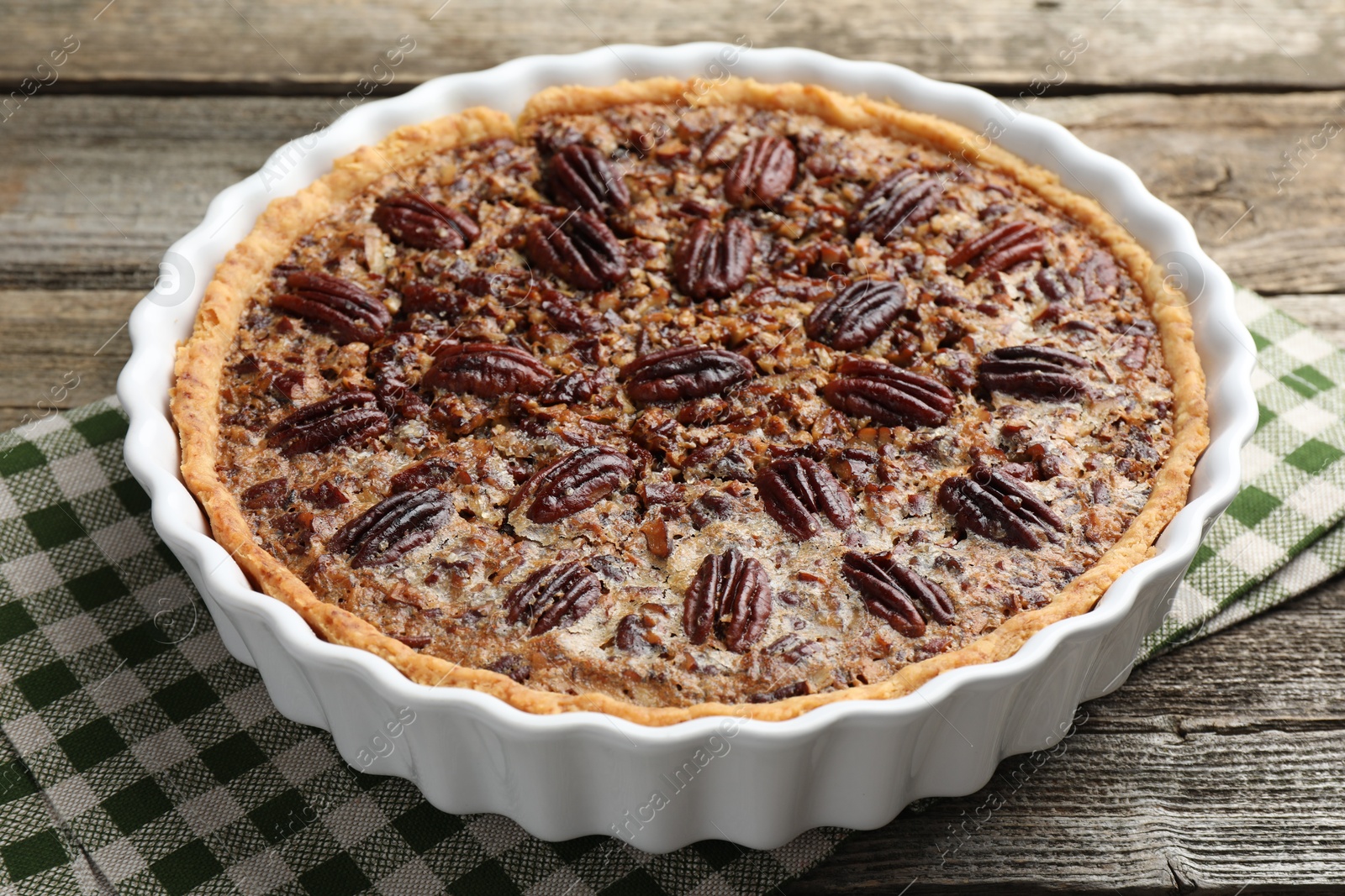 Photo of Delicious pecan pie in baking dish on wooden table, closeup