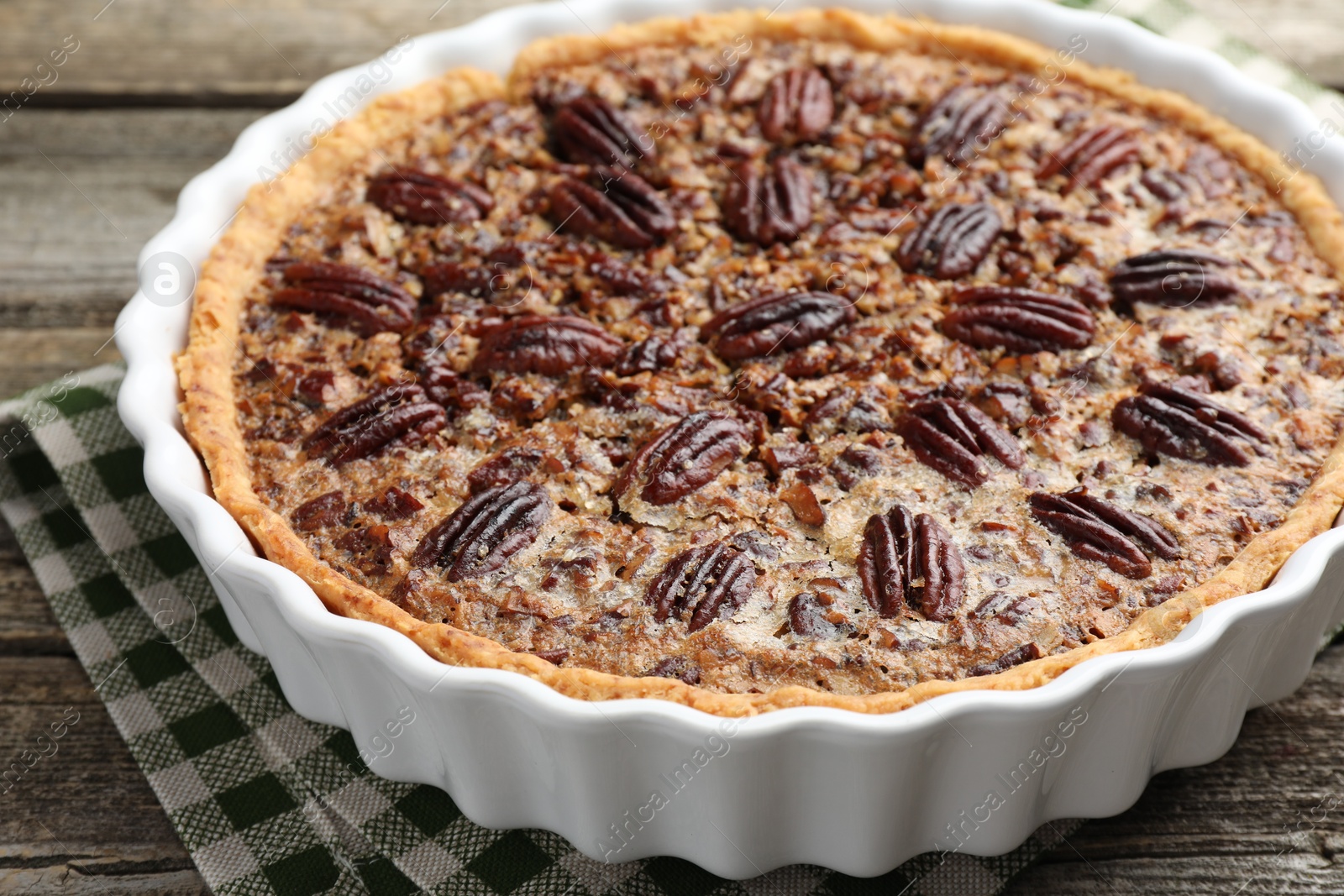 Photo of Delicious pecan pie in baking dish on wooden table, closeup