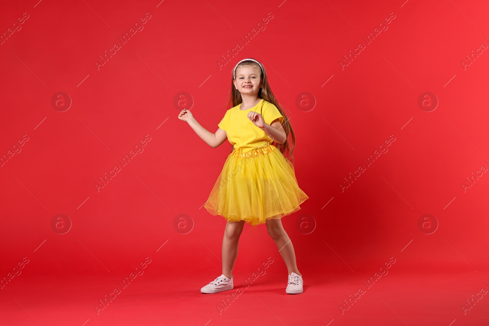 Photo of Cute little girl dancing on red background