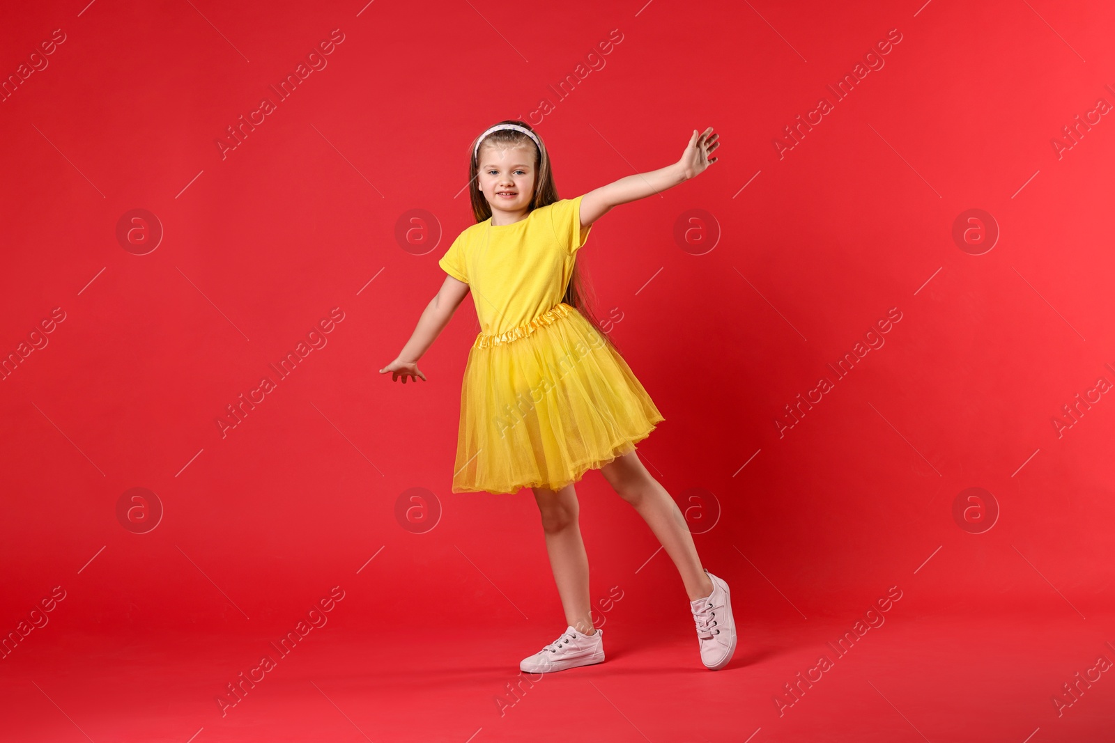 Photo of Cute little girl dancing on red background