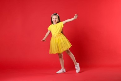 Photo of Cute little girl dancing on red background