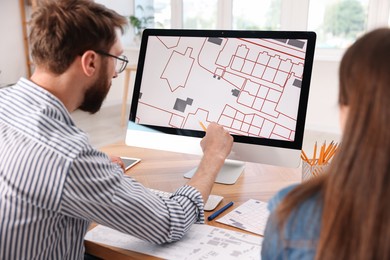 Cartographers working with cadastral map on computer at table in office, back view