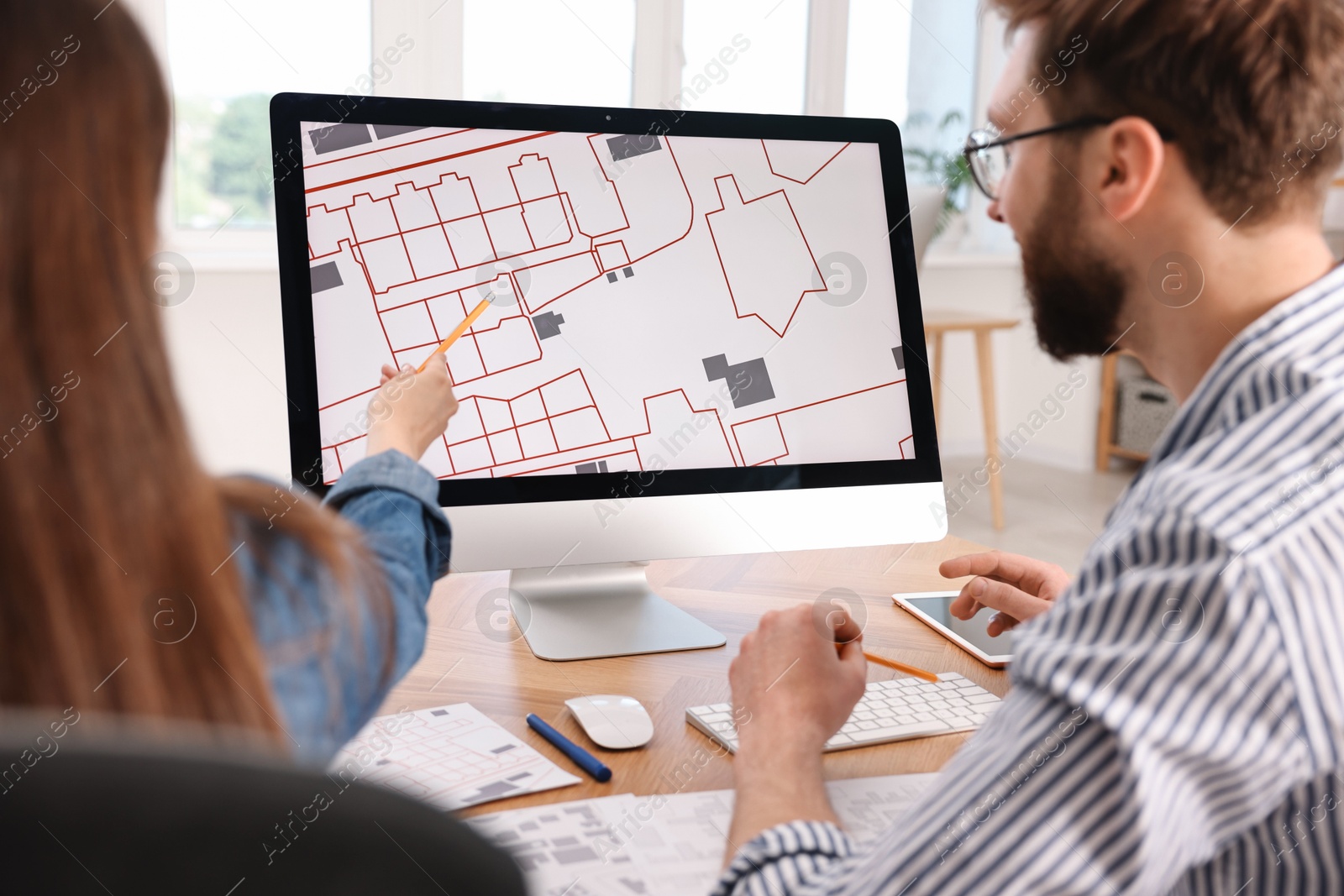 Photo of Cartographers working with cadastral map on computer at table in office, back view